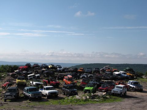1979 Ford Bronco - A large gathering of Ford Broncos and similar SUVs parked on a rocky incline, with a clear blue sky overhead.