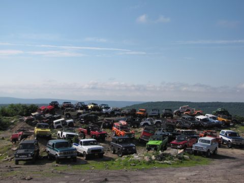 1979 Ford Bronco - A large gathering of off-road vehicles, including a 1979 Ford Bronco, are parked on a grassy hill on a sunny day.