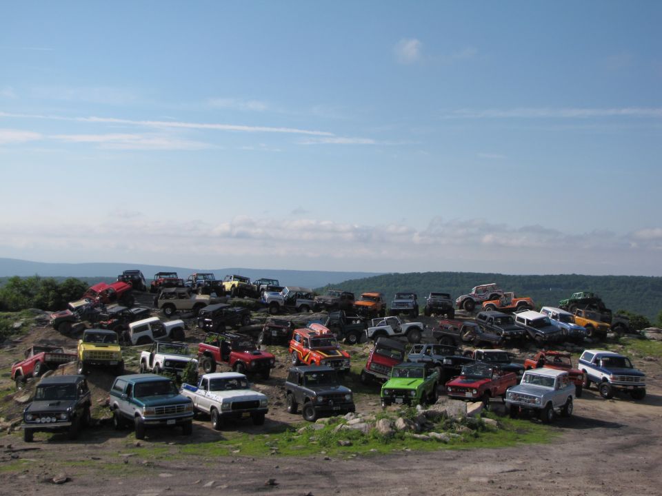 Many Ford Broncos and other SUVs parked on a hill under a blue sky