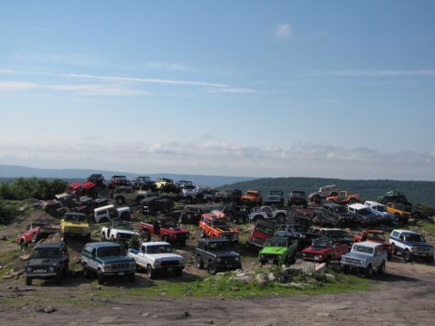 1979 Ford Bronco - A large gathering of off-road vehicles are parked on a hillside, with a scenic view of distant hills and clouds.