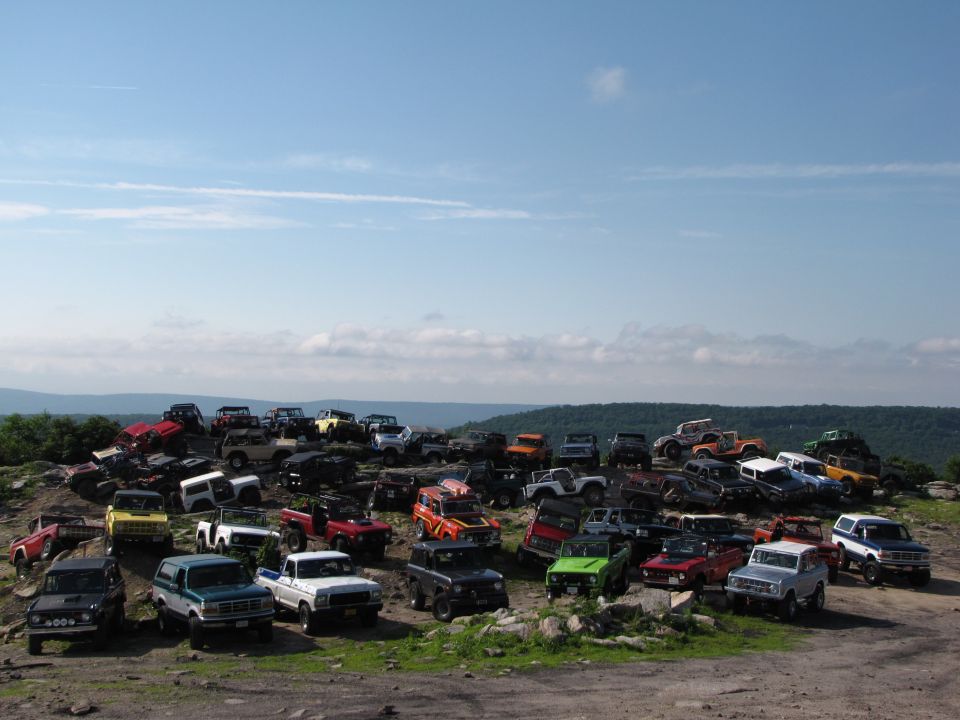 Many Ford Broncos and other SUVs parked on a rocky hillside under a blue sky