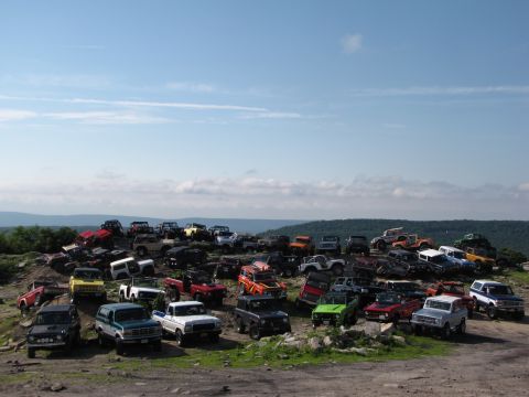 1979 Ford Bronco - A large group of off-road vehicles are gathered on a rocky terrain under a clear blue sky.