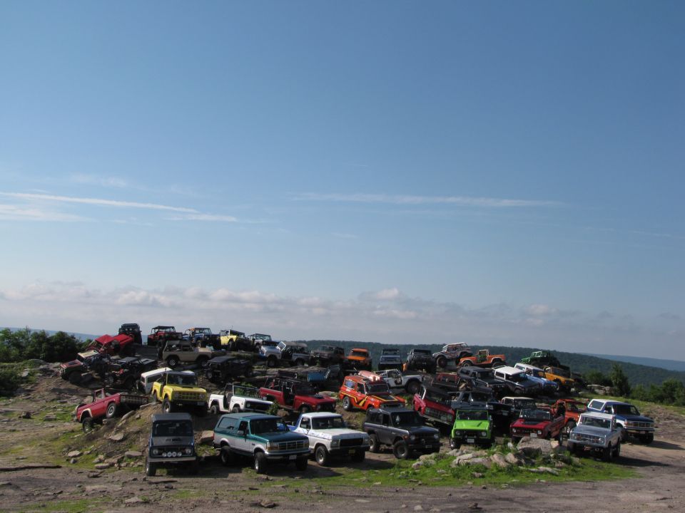 Many SUVs and trucks parked on a rocky hill under a blue sky
