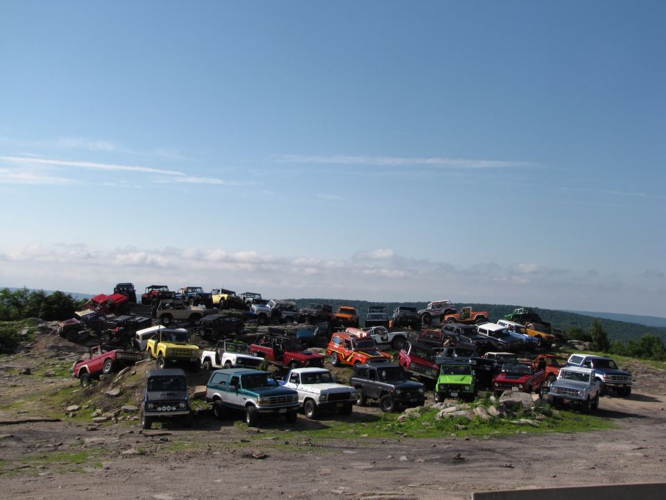 Many off-road vehicles parked on a rocky hill under a blue sky