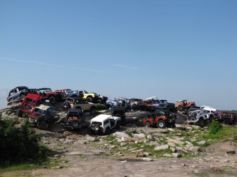 1979 Ford Bronco - A large group of off-road vehicles are gathered on a rocky incline on a sunny day.