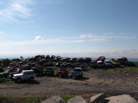1979 Ford Bronco - A collection of off-road vehicles, including a silver 1978 Ford Bronco, are parked on a hill under a blue sky.
