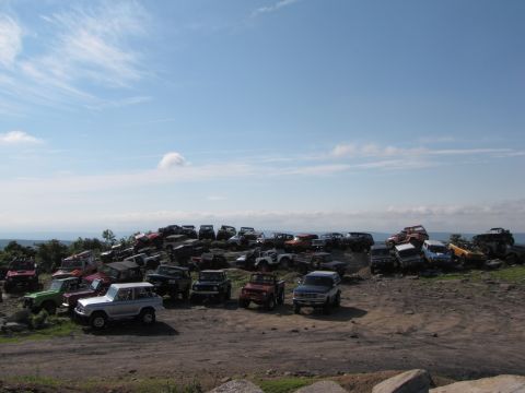 1979 Ford Bronco - A large collection of off-road vehicles are gathered on a grassy, rocky incline.