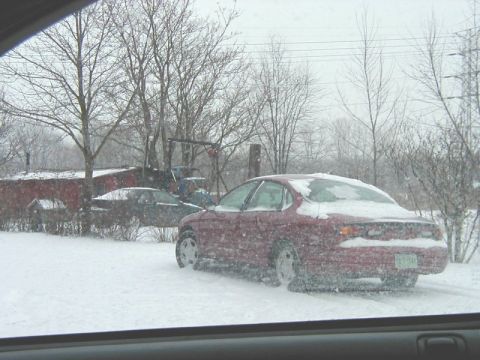 1997 Ford Taurus - Two cars are parked outside during a snowstorm, with one red sedan in the foreground.