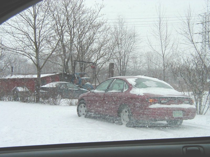 red sedan parked in snow, another car in background