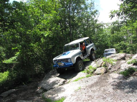 1979 Ford Bronco - A white and blue 1979 Ford Bronco navigates a challenging rocky terrain, with another vehicle visible in the background.