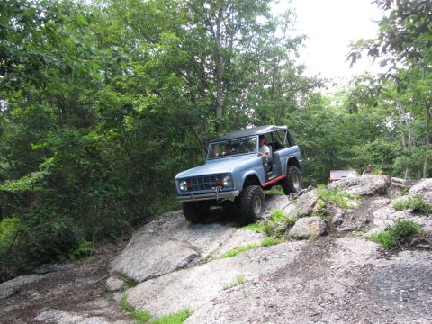 1979 Ford Bronco - Off-road vehicle navigates a rocky terrain with trees surrounding the path.