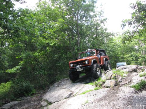 1979 Ford Bronco - An orange off-road SUV navigates a rocky trail, with another vehicle visible in the background.