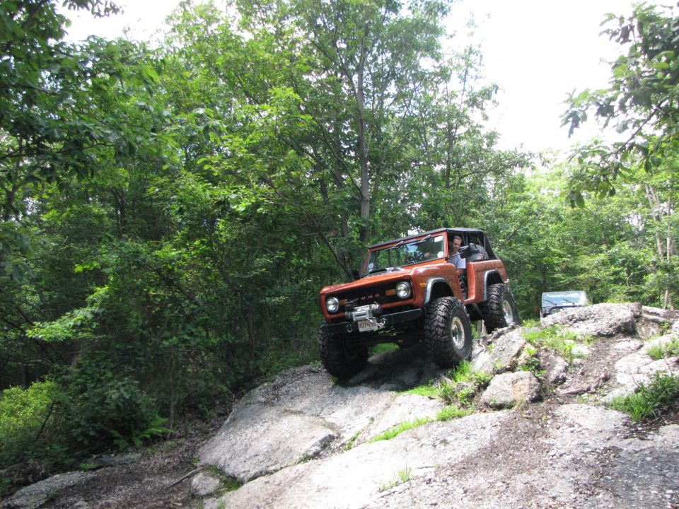 Orange off-road SUV with large tires climbing rocks, winch on front bumper, soft top