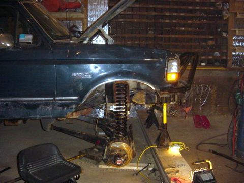 1992 Ford Bronco - The front quarter of a dark green 1992 Ford Bronco is visible with the hood up and front wheel removed for repairs.