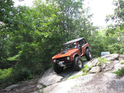 1979 Ford Bronco - Orange 1979 Ford Bronco navigating a rocky off-road trail with another vehicle behind it.