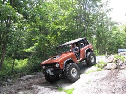 1979 Ford Bronco - A modified 1978 Ford Bronco navigates a challenging off-road course surrounded by dense woods.