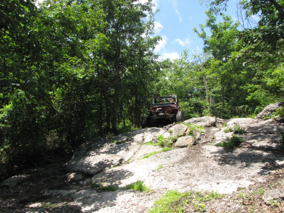 red Jeep climbing rocky trail in woods