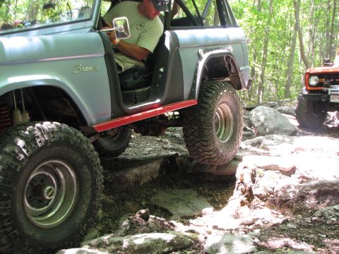 1979 Ford Bronco - Two off-road vehicles tackle a challenging rocky path in a wooded area.