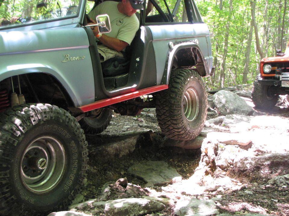 Two off-road vehicles navigating a rocky trail, one is a light blue SUV with red trim