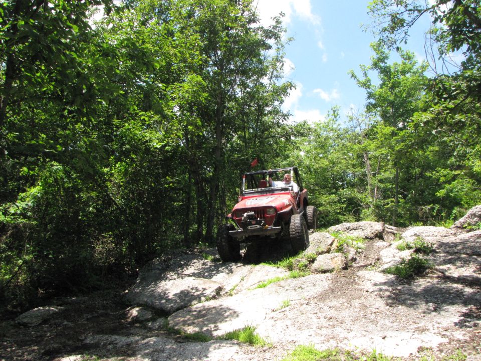Red Jeep Wrangler driving over rocks on a wooded trail