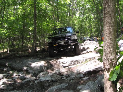 1979 Ford Bronco - A black SUV tackles a challenging off-road course with other vehicles visible in the background.