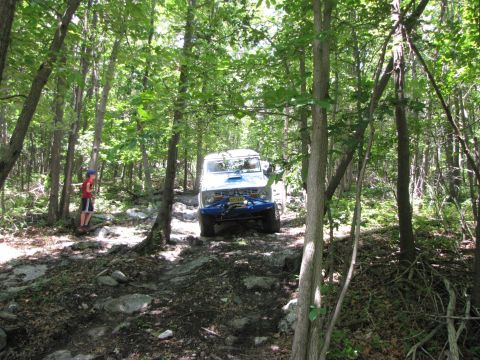 1979 Ford Bronco - An off-road vehicle navigates a challenging, wooded trail with many rocks and uneven terrain.