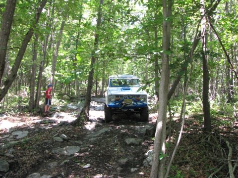 1979 Ford Bronco - A white 1978 Ford Bronco navigates a challenging rocky trail through a dense forest.