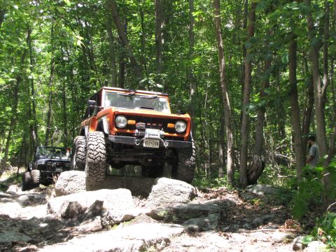 1979 Ford Bronco - An orange 1979 Ford Bronco navigates a rocky trail with a second vehicle following behind in a wooded area.