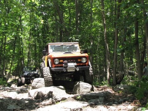 1979 Ford Bronco - An orange 1978 Ford Bronco navigates a rocky trail, with another vehicle following behind in the woods.