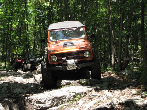 1979 Ford Bronco - Off-road vehicles, including a 1979 Ford Bronco, traverse a challenging rocky path through a wooded area.