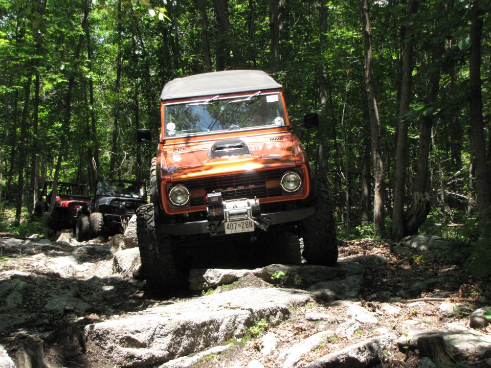 1979 Ford Bronco navigating rocky trail with other off-road vehicles behind it