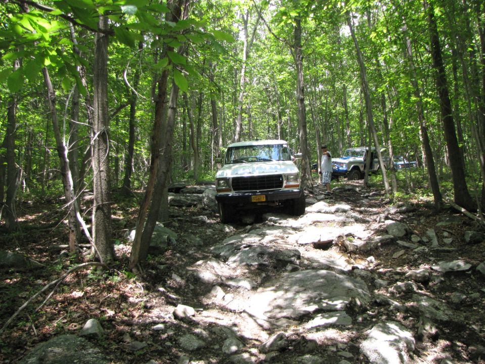 White 1987 Ford Bronco on a rocky forest trail with another SUV behind it