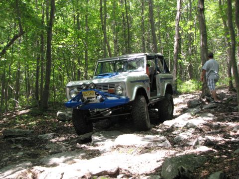 1979 Ford Bronco - A modified Ford Bronco navigates a challenging off-road path through a dense forest.