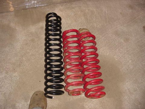 1992 Ford Bronco - Two sets of suspension coil springs, one black and two red, are laid out on a concrete surface.