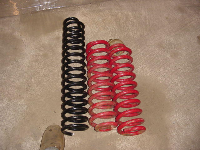 black coil spring next to two red coil springs on concrete floor