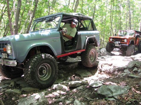 1979 Ford Bronco - Two Ford Broncos navigate a challenging rocky path through a wooded area.