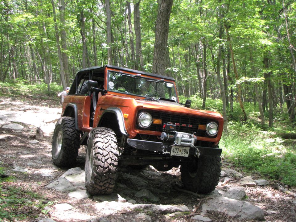 Orange SUV with large tires on a rocky trail in the woods. License plate reads 407-28N
