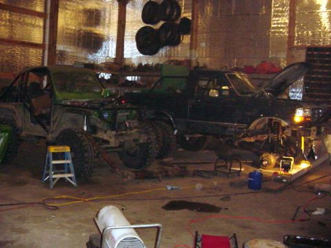1992 Ford Bronco - Two modified off-road vehicles are undergoing work in a cluttered garage setting.