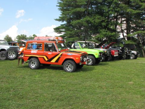 1979 Ford Bronco - An orange 1979 Ford Bronco, decorated as an emergency vehicle, is displayed with other trucks on a grassy field.