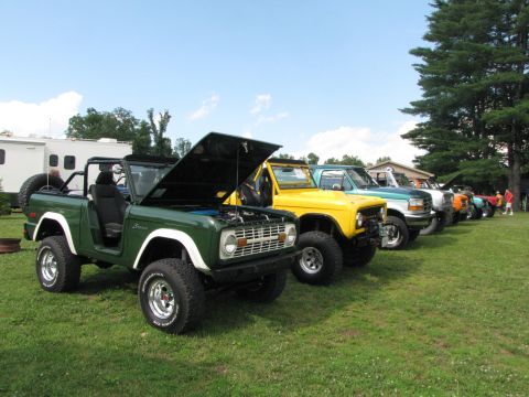 1979 Ford Bronco - Several off-road vehicles, including a green Bronco, are lined up on a grassy field under a blue sky.
