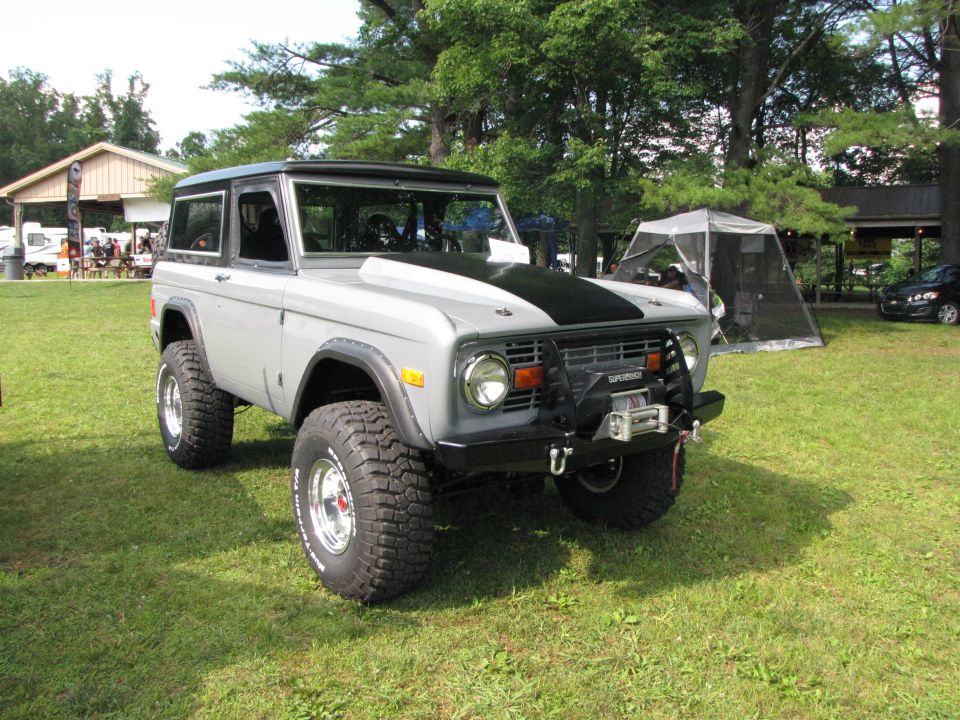 Gray 1978 Ford Bronco with black hood stripe, lifted suspension, and winch on front bumper parked on grass
