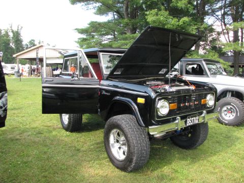 1979 Ford Bronco - A black 1979 Ford Bronco is displayed with its hood and driver's door open, parked on a grassy field next to another vehicle.
