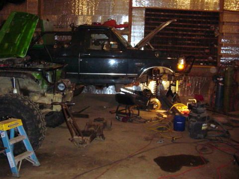 1992 Ford Bronco - A dark green SUV is in a garage with its hood open, undergoing mechanical work. Another vehicle is partially visible to the left.