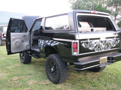 1979 Ford Bronco - This black Ford Bronco features custom skull graphics and aftermarket wheels, with its driver's door open.