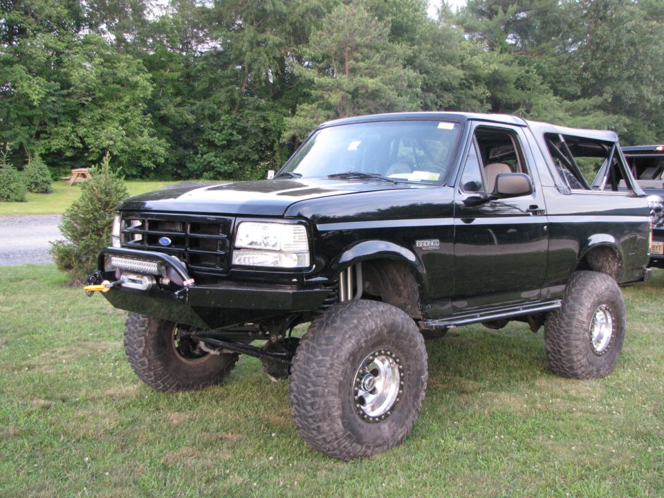 Black lifted Ford Bronco with aftermarket bumper, winch, and roll cage visible