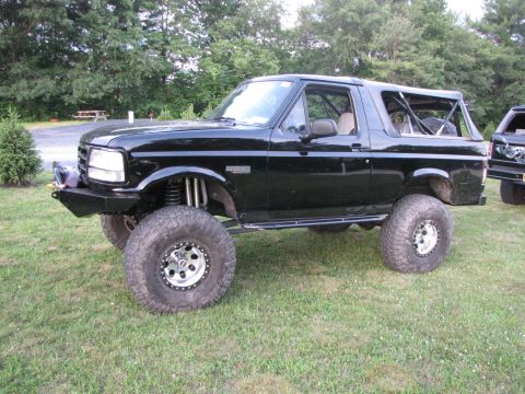 1979 Ford Bronco - A heavily modified black Ford Bronco is parked outdoors on a grassy area, with another vehicle visible in the background.