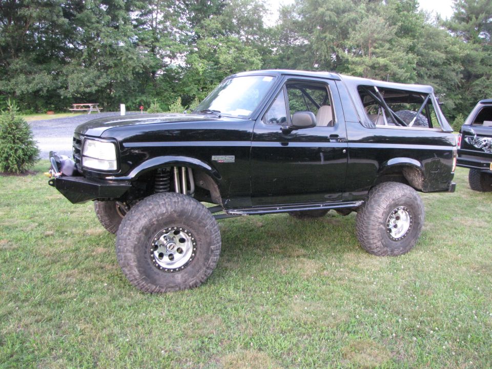 Lifted black Ford Bronco with large tires and custom bumper parked on grass
