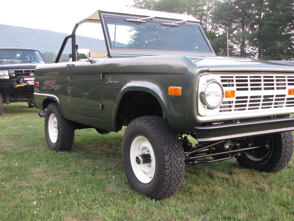 Green Ford Bronco parked on grass, another black SUV behind it