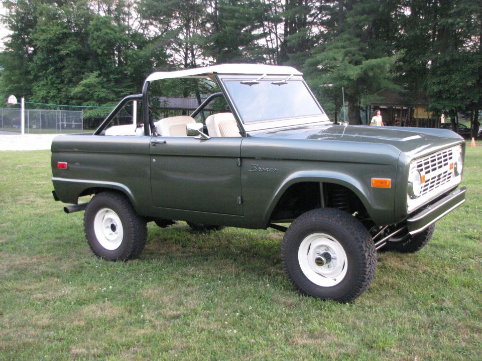 Green 1979 Ford Bronco with white wheels and soft top, parked on grass