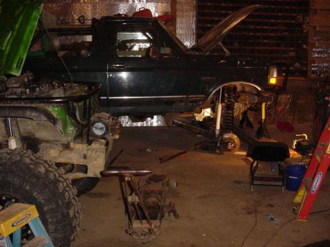 1992 Ford Bronco - A dark green 1992 Ford Bronco is undergoing repairs indoors, with its front end lifted and suspension components removed.